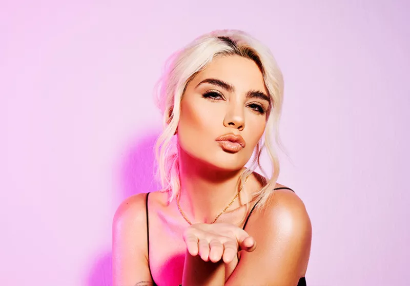 Woman looking straight into the camera blowing a kiss on a pink background